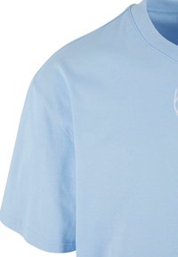 T-shirt en coton bleu clair avec une texture douce, col rond et manches courtes. Présente un design brodé discret sur la poitrine.
