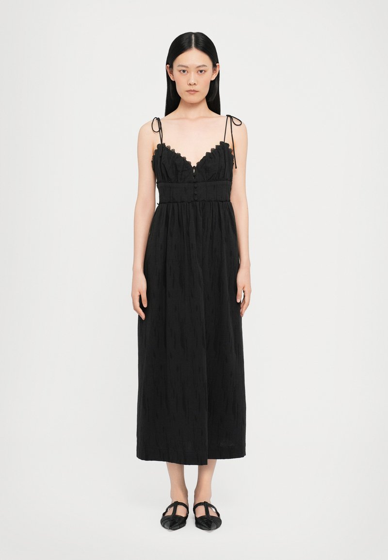 Schwarzes Maxikleid mit Spitze und verstellbaren Spaghettiträgern, mit Knopfverschluss und strukturiertem Stoff. Das Modell trägt flache schwarze Schuhe.