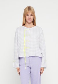 Lysegrå ternet oversized skjorte med lange ærmer, rund halsudskæring og neon-gule tryklåsdetaljer. Matches med lavendelfarvede kordfløjlsbukser.