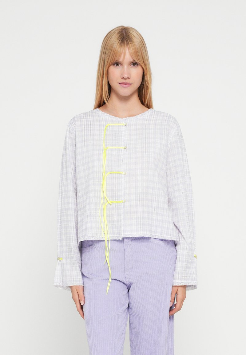 Lysegrå ternet oversized skjorte med lange ærmer, rund halsudskæring og neon-gule tryklåsdetaljer. Matches med lavendelfarvede kordfløjlsbukser.
