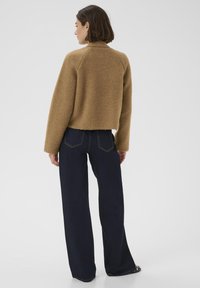 Maglione marrone peloso con maniche raglan, lunghezza corta, abbinato a jeans blu scuro a gamba larga. Design minimalista e testurizzato.