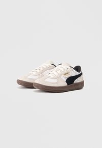 Puma sportcipő bézs velúrból és fehér textilből készült felsőrésszel, fekete velúr díszítéssel és barna gumitalppal. Fűzős kialakítás logó részlettel.