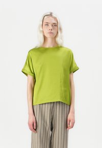 Green short-sleeve blouse with a loose fit, round neckline, and smooth texture. Paired with striped wide-leg trousers.