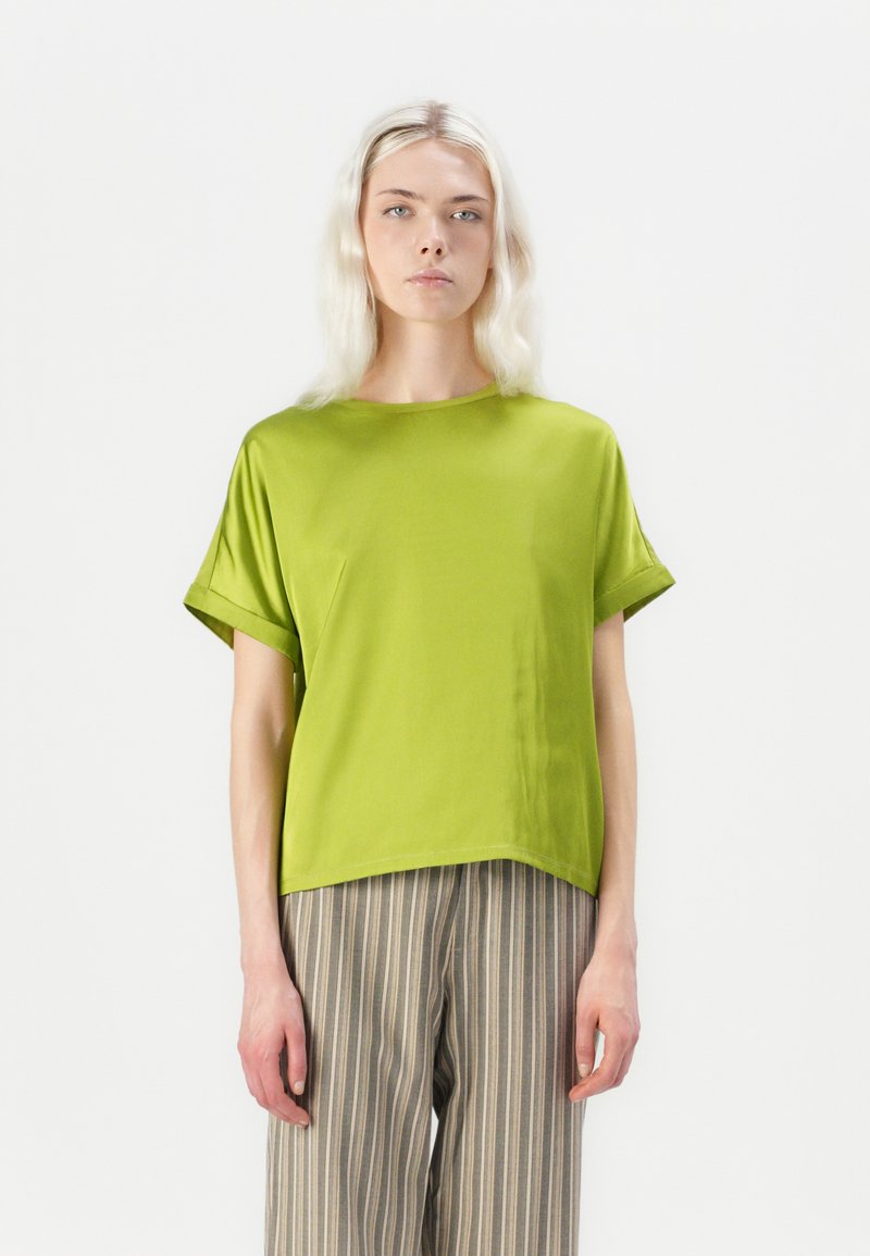 Green short-sleeve blouse with a loose fit, round neckline, and smooth texture. Paired with striped wide-leg trousers.