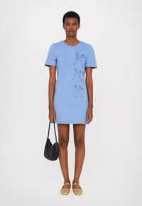 Light blue denim mini dress with short sleeves, featuring decorative bows and contrasting stitching. Paired with a black woven handbag.