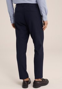 Tengerészkék, slim fit nadrág rugalmas derékkal és két hátsó zsebbel; fekete cipővel párosítva, sima felülettel.