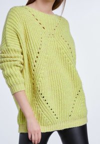 Pull tricoté surdimensionné vert citron avec des poignets et une taille côtelés, présentant des détails en maille ouverte et une coupe ample.