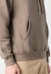 Sudadera beige con un bolsillo tipo canguro, capucha con cordón, puños y dobladillo de canalé. Tejido suave con una textura lisa. Diseño sencillo y casual.