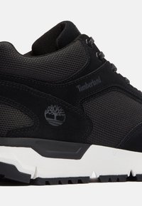 Černé tenisky s síťovinovým svrškem, semišovými detaily a bílou gumovou podrážkou. Obsahují logo Timberland a strukturovaný vzor na textilu.