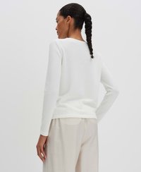 Weißer, strukturierter Pullover mit rundem Ausschnitt und langen Ärmeln, getragen über leichten, fließenden beigen Hosen, die ein einfaches, minimalistisches Design präsentieren.