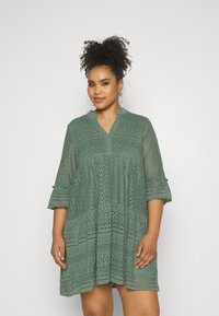 Grünes Spitzenkleid mit V-Ausschnitt, Dreiviertelärmeln und einem weit schwingenden Design, verziert mit aufwändigen Mustern und Details.