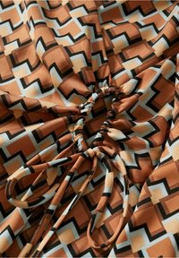 Tissu avec un motif géométrique en zigzag orange, beige, noir et blanc, rassemblé au centre avec un cordon noué en un nœud.