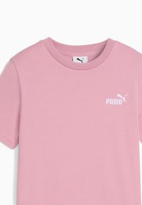 Rožinė medvilninė marškinė su apvaliu kaklu, trumpomis rankovėmis ir balta Puma logo, siuvinėta ant kairės krūtinės. Lygus paviršius, įprastas kirpimas.
