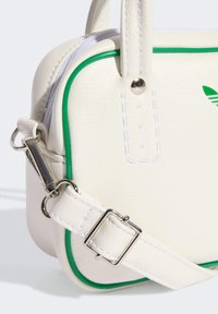 Bílá kožená taška se zelenými akcenty, s horními držadly a nastavitelným popruhem. Obsahuje stříbrné kování a prošité detaily kolem okrajů.