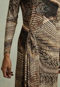 Rochie cu mâneci lungi, având un model de piele de șarpe în nuanțe de maro și bej. Țesătura se lasă elegant, cu un detaliu strâns pe lateral.