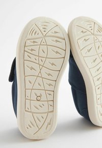 Schuhe aus navy-blauem Stoff mit einer weißen Gummisohle, die ein strukturiertes Grip-Muster aufweist, und einem Klettverschluss für sicheren Halt.