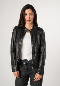 Schwarze Lederjacke mit einem Reißverschluss vorne, rundem Kragen und strukturierten Schultern, kombiniert mit dunkelgrauen Jeans und einem weißen Hemd darunter.