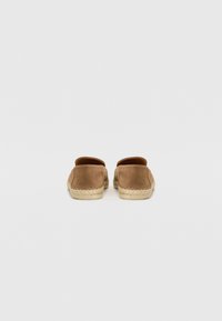 Bruna mockaskor med en vävd jutesula, baklös design och sydda detaljer längs kanten. Enkel och minimalistisk stil.