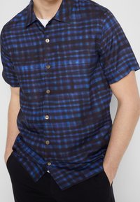 Korte mouw overhemd in een donkerblauw ruitpatroon met lichtere blauwe accenten, voorzien van een knoopsluiting aan de voorkant en een gladde textuur.