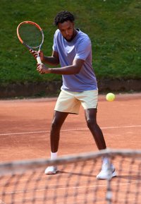 Mees lilla särk ja heledates kollastes lühikeses, hoides tennisereketit, valmistub lööma tennisepalli savimenetluses. Roheline muru taustal.