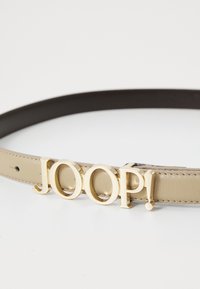 Bezová kožená opasok s prackou z kovu v zlatej farbe, na ktorej sú výrazne zobrazené písmená "JOOP!". Hladký povrch s akcentmi šitia.