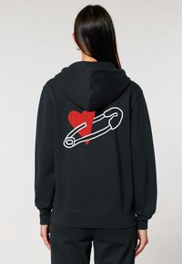 Fekete kapucnis pulóver, amelyen egy nagy piros szív és egy fehér körvonalú biztosítótű hímzett a hátsó oldalon. Puha anyag, laza szabású.