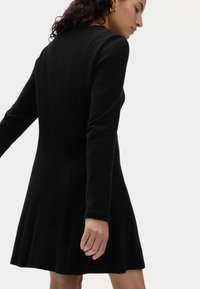 Schwarzes Kleid aus weichem Material mit langen Ärmeln, tailliertem Oberteil und ausgestelltem Rock mit dezenten Nahtdetails.