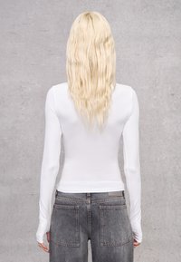 Wit shirt met lange mouwen en een getailleerd ontwerp, gecombineerd met hooggetailleerde grijze jeans met een klassieke snit en twee achterzakken.