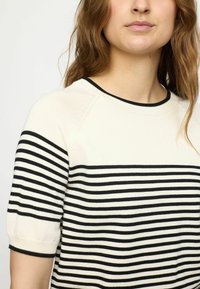 Gestreifter Pullover mit geripptem Rundhalsausschnitt, kurzen Ärmeln und horizontalen schwarzen und cremefarbenen Streifen über dem Körper.