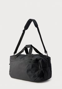 Mustasta kestävästä kankaasta valmistettu duffel-laukku, jossa on kahdet yläkahvat, säädettävä olkahihna ja vetoketjullinen etutasku.