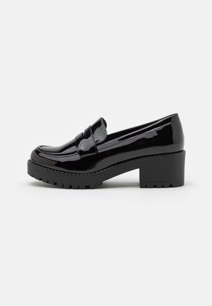 Czarny lakierowany loafers na masywnym obcasie z żłobioną podeszwą, w stylu wsuwanych butów, widok z boku na gładkim jasnym tle.