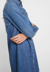 Denimskjortklänning i ljusblått. Har en knappstängning fram, bröstficka och långa ärmar. Tyget har en lätt texturerad yta.