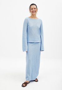 Svetlo modra pletena obleka, ki vključuje dolge rokave in usklajen dolg krilo. Ima teksturirano tkanino z valovitim vzorcem.