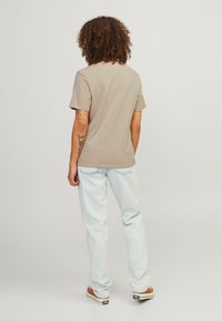 Beige katoenen t-shirt met korte mouwen, gecombineerd met lichtblauwe denim jeans. De outfit heeft subtiele stiksels en casual schoenen.