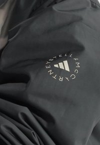 Tissu noir avec un logo circulaire blanc contenant trois barres ascendantes et des lettres disposées autour.