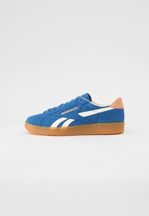 Blauer Wildleder-Reebok-Sneaker mit weißen Streifen und Gummisohle, von der Seite auf weißem Hintergrund gesehen.