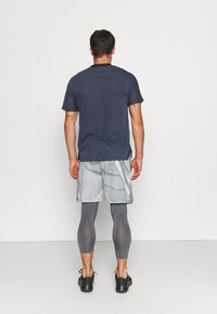 Camisa de manga corta azul marino con tejido texturizado, combinada con pantalones cortos de patrón gris claro y leggings grises, zapatos negros visibles.