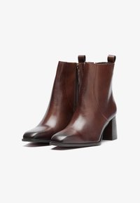 Brown leather ankle boots with a pointed toe, side zipper, and a chunky heel. Smooth texture with minimal detailing and a pull tab.