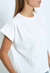 Bílý krátký rukáv tričko vyrobené z bavlny, s uvolněným střihem, se subtilními záhyby na rukávech a kulatým výstřihem.
