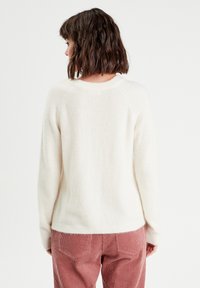Pull en laine couleur crème avec un col rond, des manches raglan et un ourlet côtelé, associé à un pantalon en velours côtelé rose. Tissu doux et texturé.