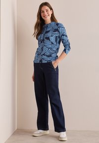 Modrá a námořnická patterned dlouhá košile s kulatým výstřihem, doplněná tmavými denimovými kalhotami rovného střihu a bílými teniskami.