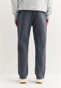 Szare bawełniane spodnie o prostym kroju, z dwoma tylnymi kieszeniami i kontrastującymi przeszyciami, zestawione z białymi trampkami.