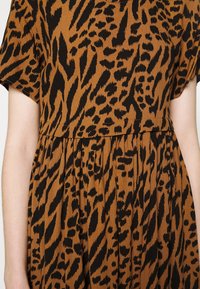 Klädsel med djurmönster i brunt och svart, kortärmad och samlad i midjan, visad från övre torso.