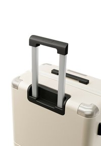 Harde koffer in off-white met zilveren accenten, voorzien van een zwarte telescopische handgreep, een gestructureerd oppervlak en versterkte hoeken.