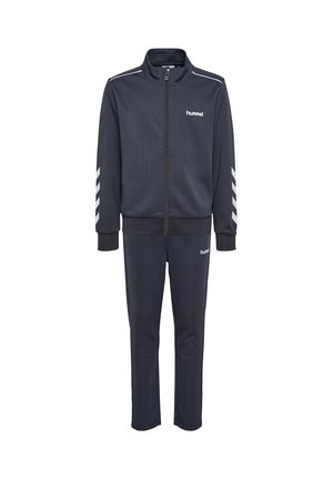 Marineblauw trainingspak met ritsvest en broek, witte hummel-logo's op borst en dij, en witte chevronstrepen op de mouwen.