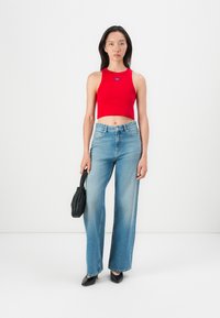 Rotes, kurzes Tanktop mit einem blauen Etikett, kombiniert mit hellblauen Weitbeinjeans, einer schwarzen Handtasche und schwarzen spitzen Schuhen.