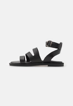 Black leather sandals featuring three wide straps, an ankle strap with a metallic buckle, and a flat sole with a subtle stitching detail.