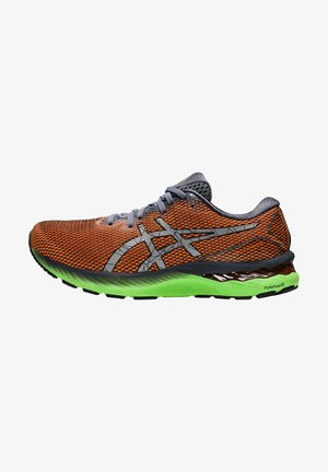 Zapatilla de correr naranja y negra con cordones grises, logo gris y suela verde brillante sobre un fondo blanco, vista lateral mostrando el lado exterior.