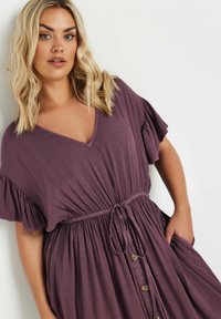 Lila, knälength klänning gjord av mjukt tyg med V-ringning, korta volangärmar, dragsko i midjan och knapppdetaljer fram.