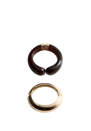 Deux bracelets larges à manchette, l'un en résine marron foncé avec un fermoir doré, l'autre en métal lisse doré avec une fermeture à charnière, sur fond blanc.